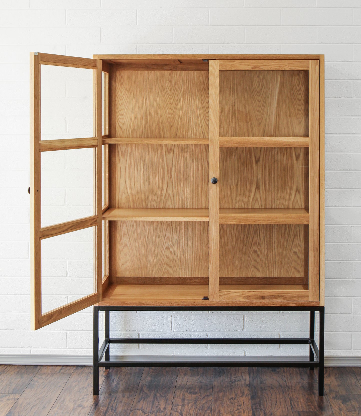 White oak display cabinet with one open door.