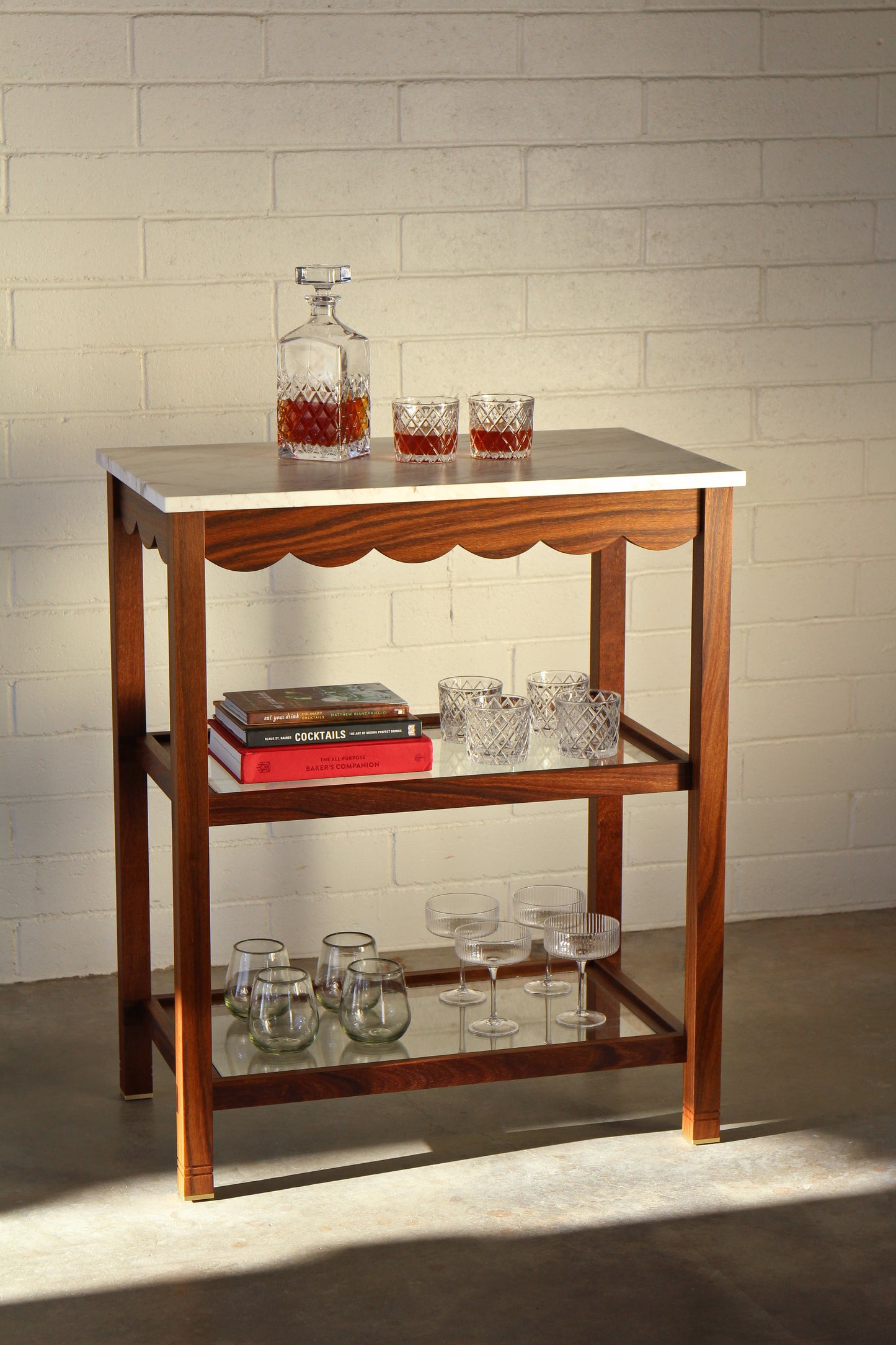 Wooden bar cart with marble top against a white brick wall