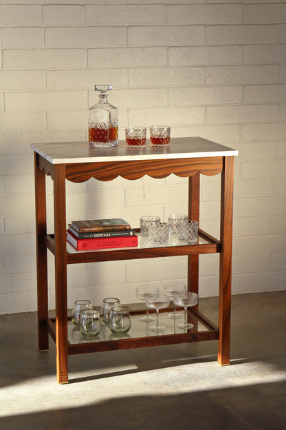 Wooden bar cart with marble top against a white brick wall