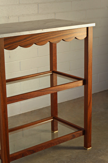 Wooden serving table with scalloped edge against a plain wall.